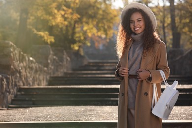 Portrait of beautiful African-American woman with stylish white backpack on stairs outdoors. Space for text