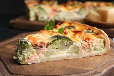 Photo of Piece of delicious homemade quiche with salmon and broccoli on wooden board, closeup