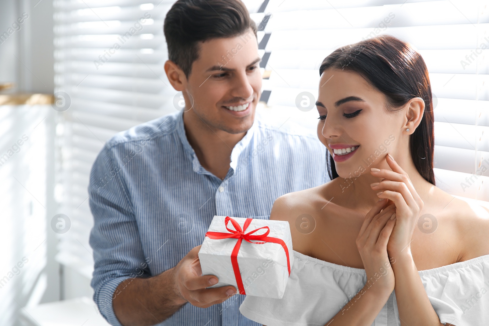 Photo of Man presenting gift to his beloved woman at home. Valentine's day celebration