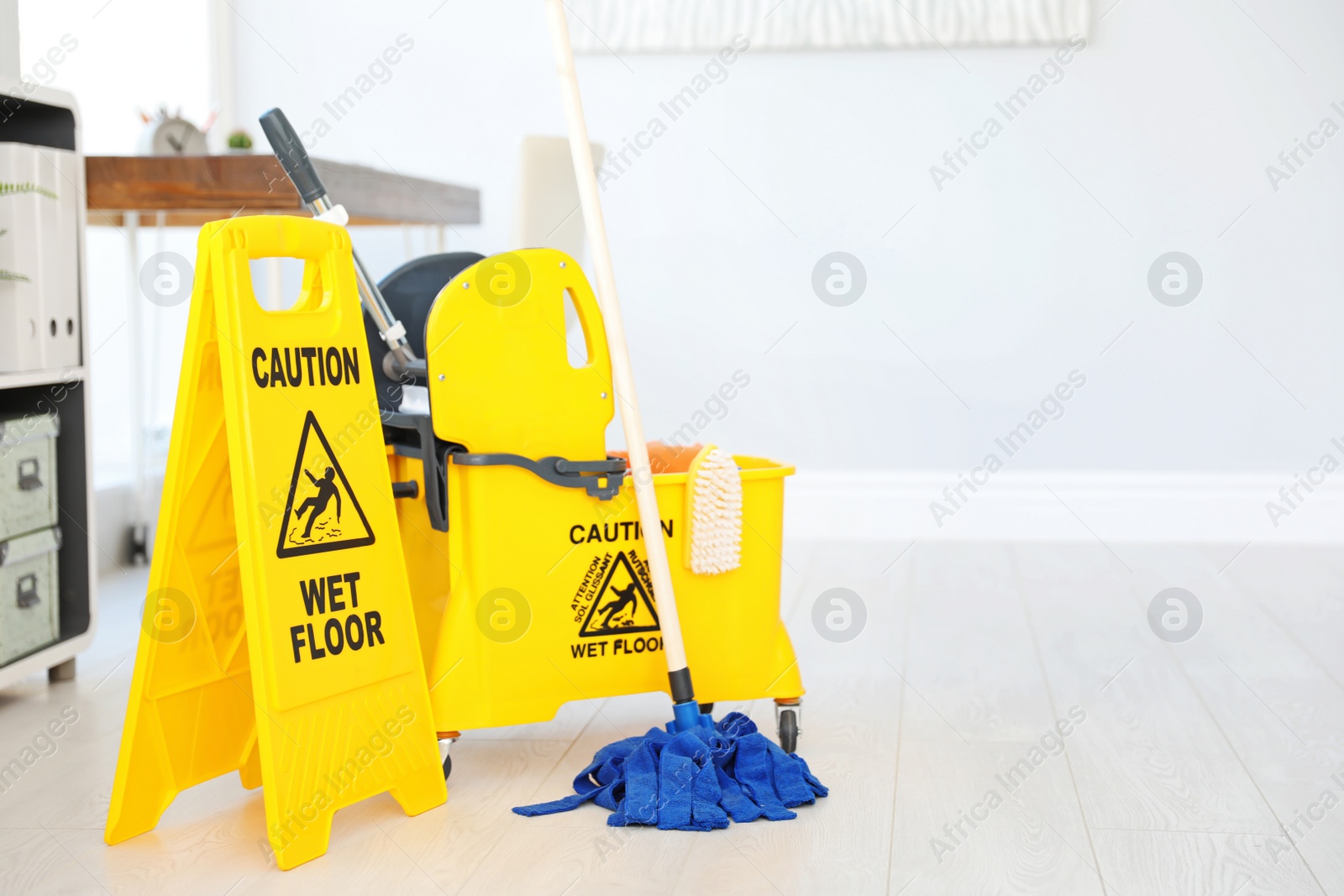 Photo of Phrase "CAUTION WET FLOOR" on safety sign and mop bucket with cleaning supplies, indoors