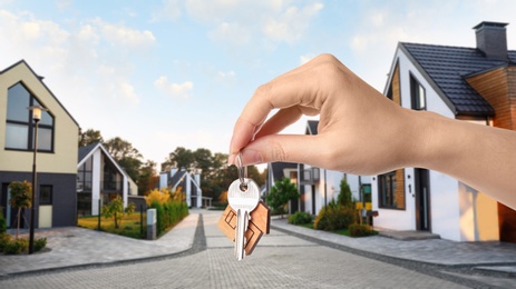 Real estate agent holding key against modern houses, closeup. Banner design