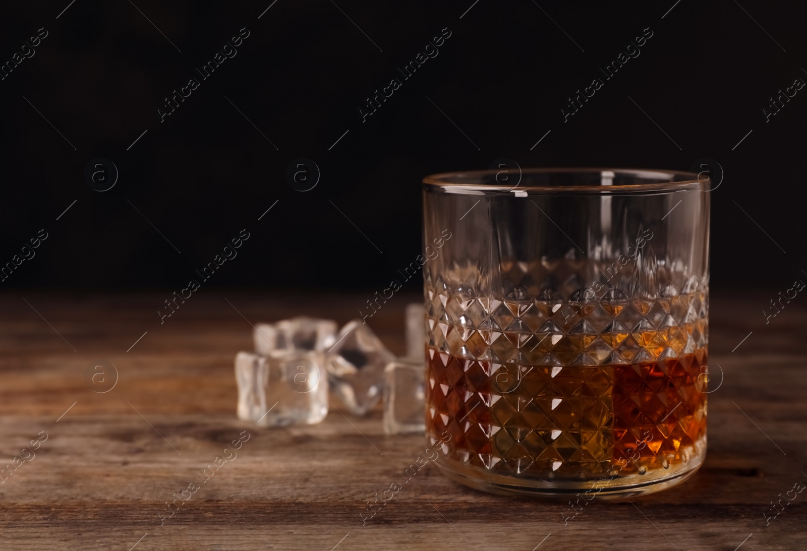 Photo of Golden whiskey in glass with ice cubes on table. Space for text