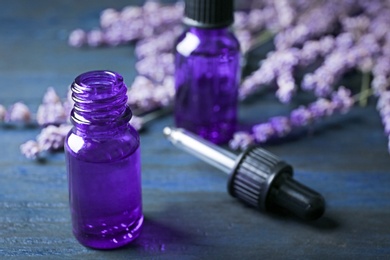 Photo of Bottles of lavender essential oil on blue wooden background