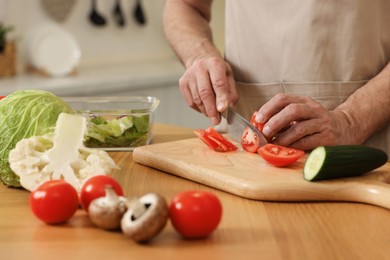 Photo of Man cutting tomato at wooden table in kitchen, closeup