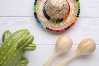 Photo of Maracas, toy cactus and sombrero hat on white wooden table, flat lay. Musical instrument