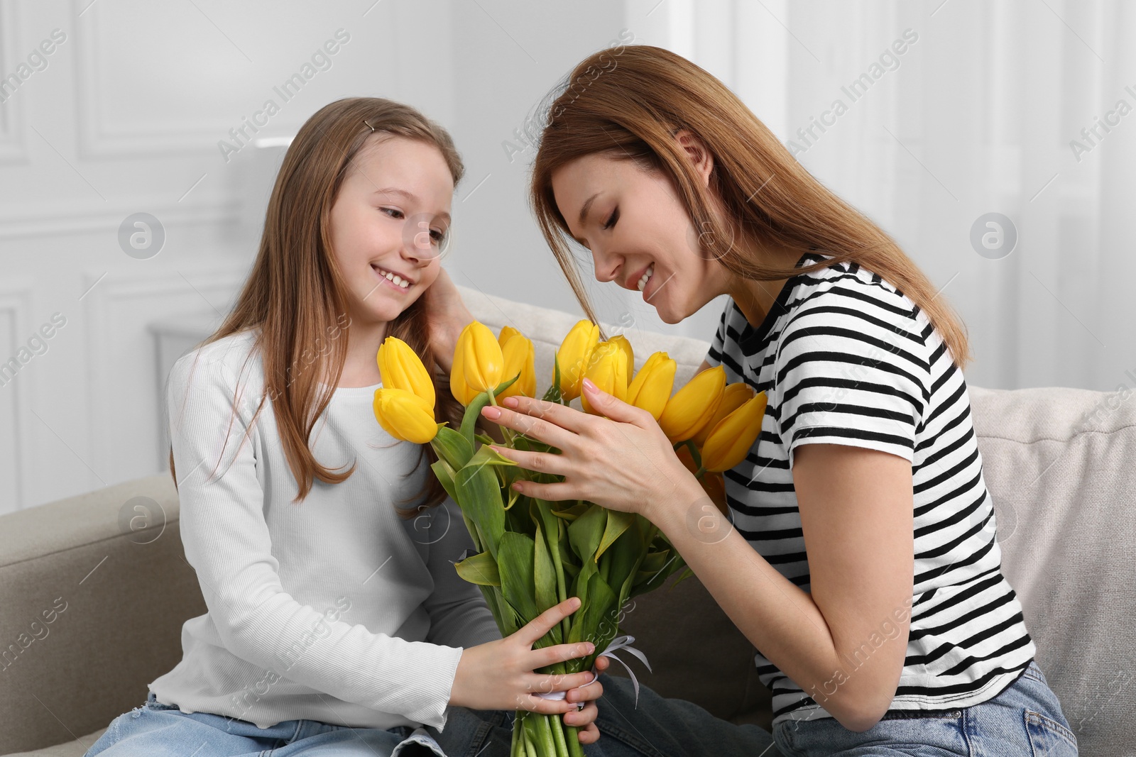 Photo of Happy mother and her cute daughter with bouquet of yellow tulips on sofa at home