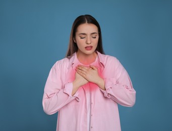 Young woman suffering from cold on blue background