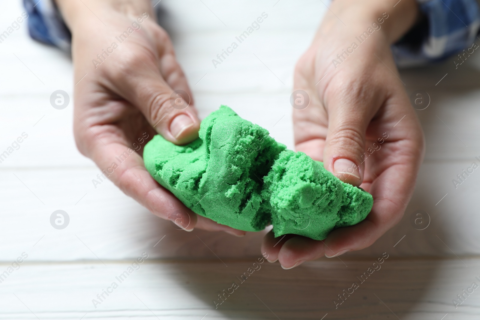 Photo of Woman playing with green kinetic sand at white wooden table, closeup