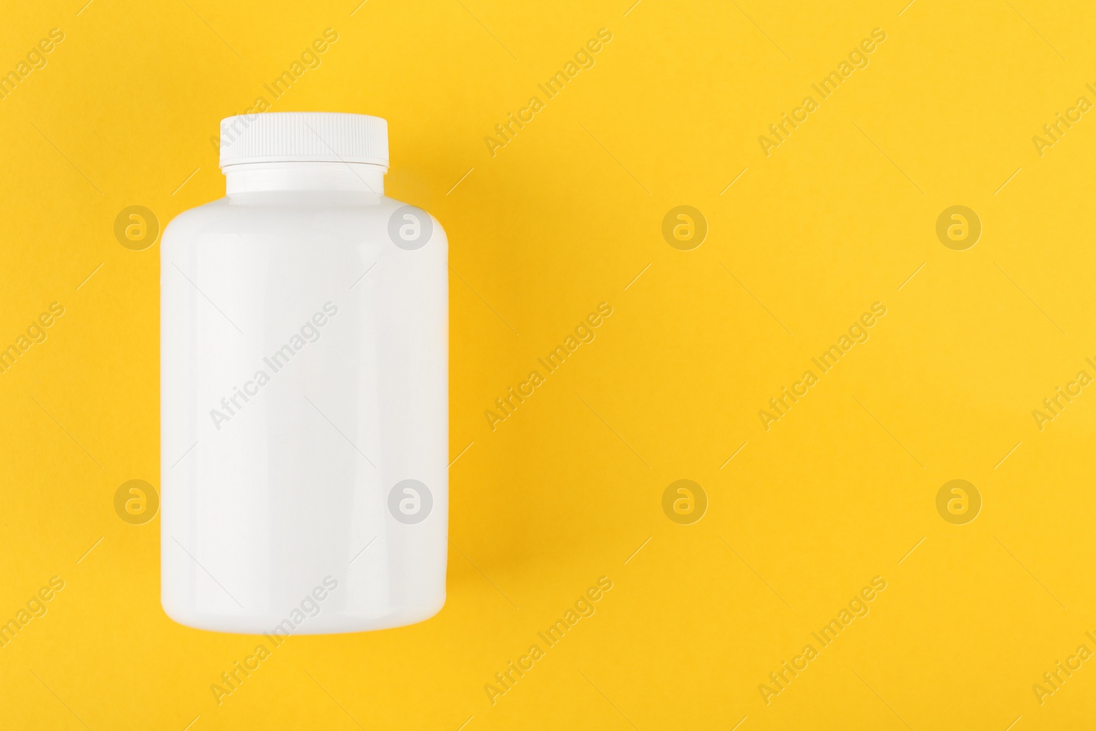 Photo of One white medical bottle on yellow background, top view. Space for text