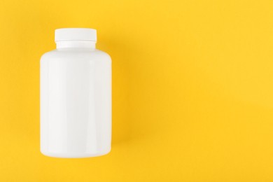 Photo of One white medical bottle on yellow background, top view. Space for text