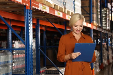 Photo of Happy manager holding clipboard in warehouse with lots of products