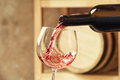 Photo of Pouring delicious red wine into glass on blurred background