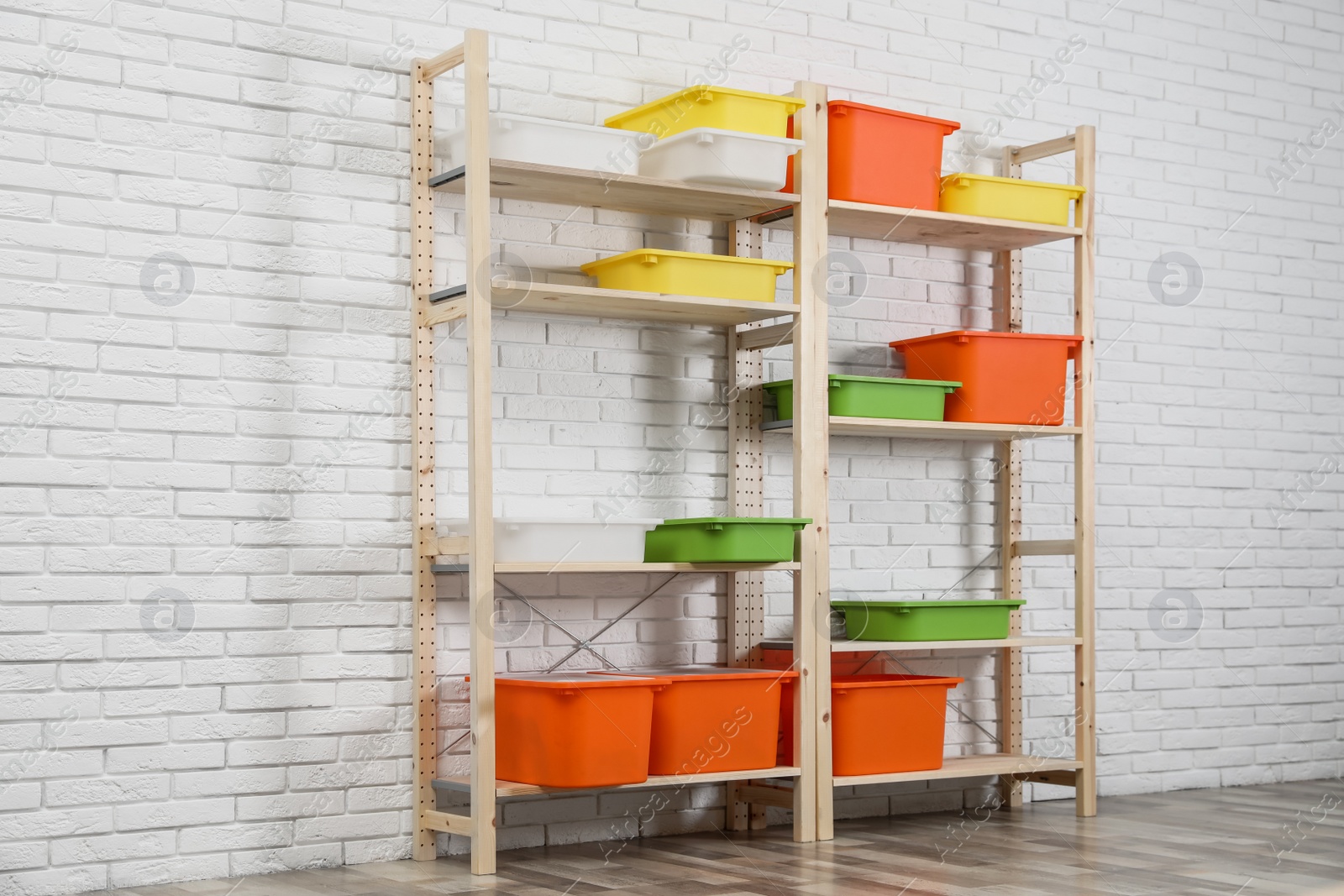 Photo of Wooden shelving units with colorful containers near white brick wall. Stylish room interior