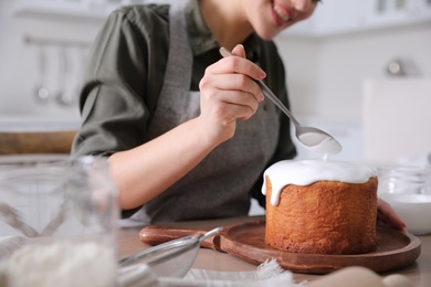 Young woman decorating traditional Easter cake with glaze in kitchen, closeup