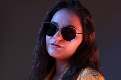 Photo of Portrait of beautiful young woman with stylish sunglasses on color background with neon lights