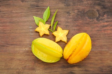 Photo of Cut and whole delicious ripe carambolas with leaves on wooden table, flat lay