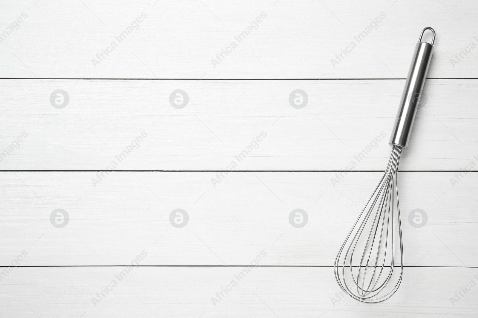 Photo of Metal whisk on white wooden table, top view. Space for text