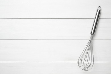 Metal whisk on white wooden table, top view. Space for text