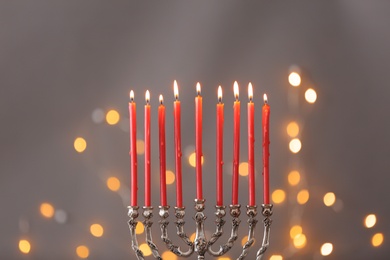 Photo of Silver menorah with burning candles against grey background and blurred festive lights. Hanukkah celebration