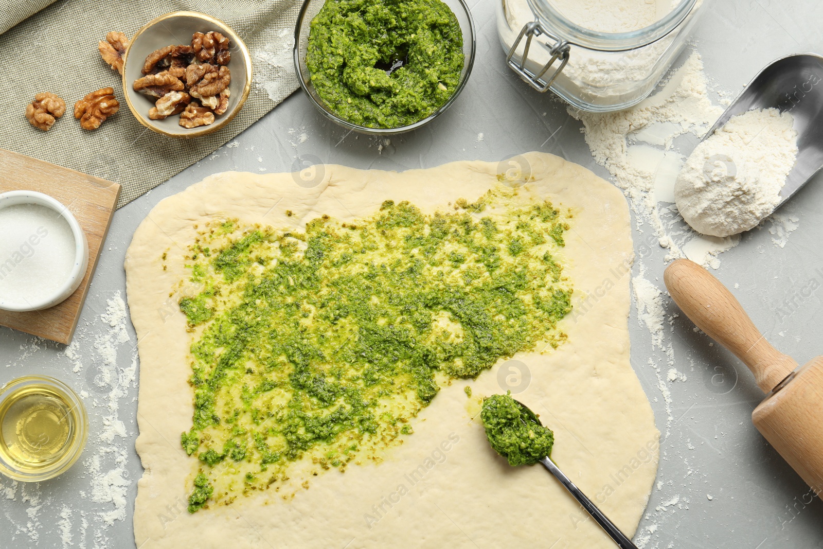 Photo of Making delicious pesto bread. Raw dough with sauce and ingredients on grey table, flat lay