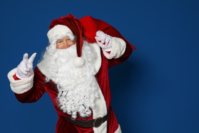 Photo of Happy authentic Santa Claus with bag full of gifts on blue background. Space for text