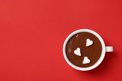 Cup of hot chocolate with heart shaped marshmallows on red background, top view. Space for text