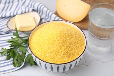 Photo of Raw cornmeal in bowl, water, cheese, parsley and butter on light table, closeup