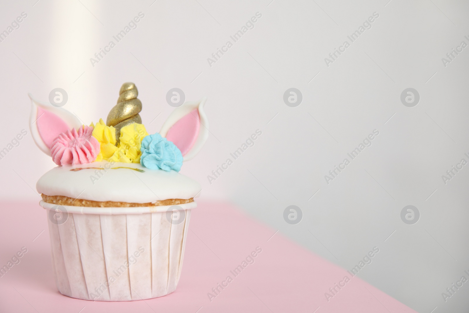 Photo of Cute sweet unicorn cupcake on pink table. Space for text