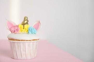 Photo of Cute sweet unicorn cupcake on pink table. Space for text