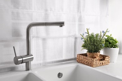 Artificial potted herbs on white marble countertop near sink in kitchen. Home decor