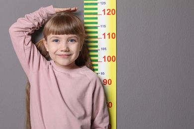 Photo of Little girl measuring her height on grey background