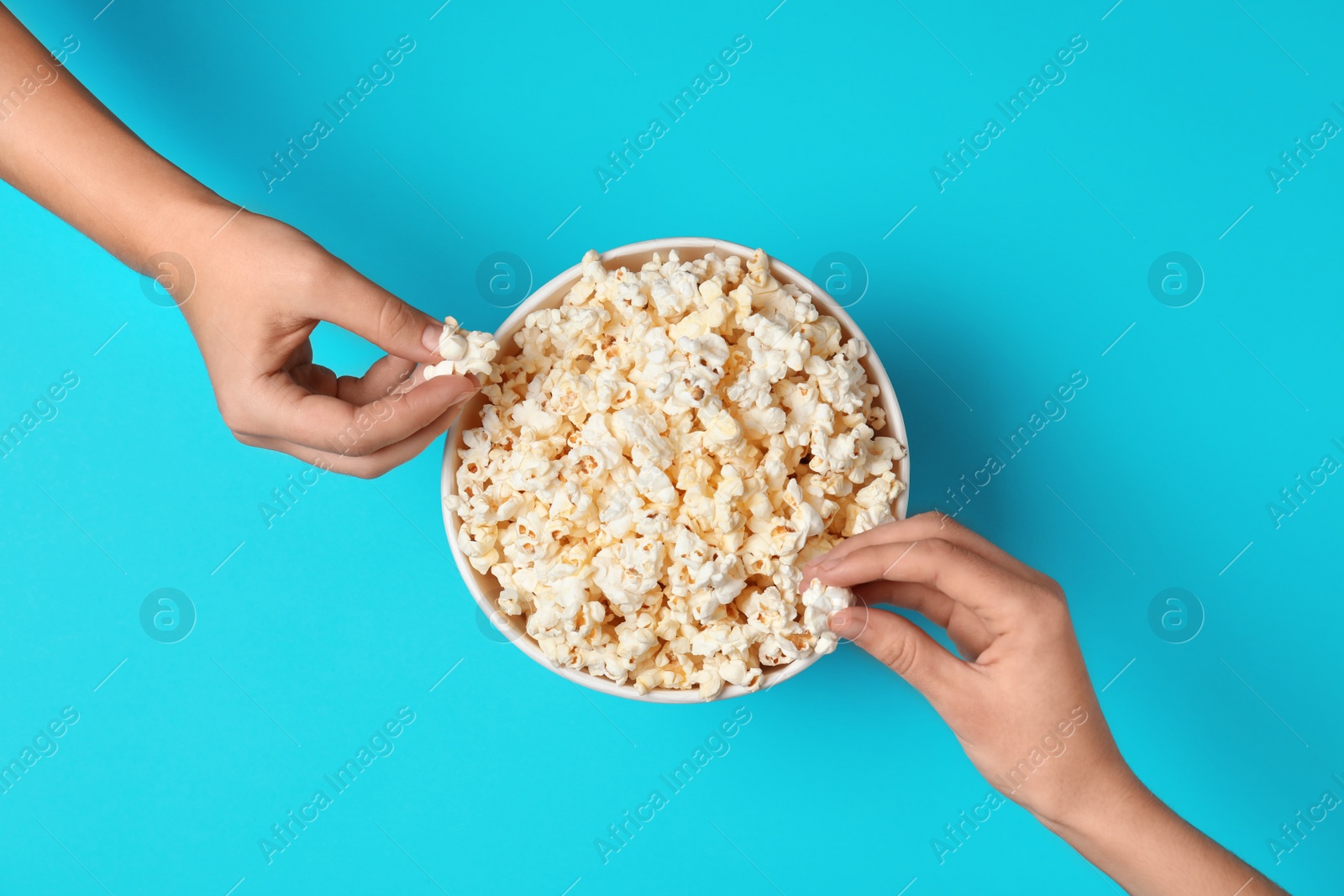 Photo of Women eating tasty popcorn from paper bucket on color background, top view