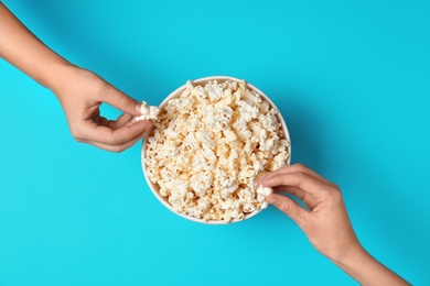 Women eating tasty popcorn from paper bucket on color background, top view