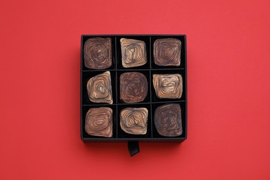 Photo of Box of tasty chocolate candies on red background, top view
