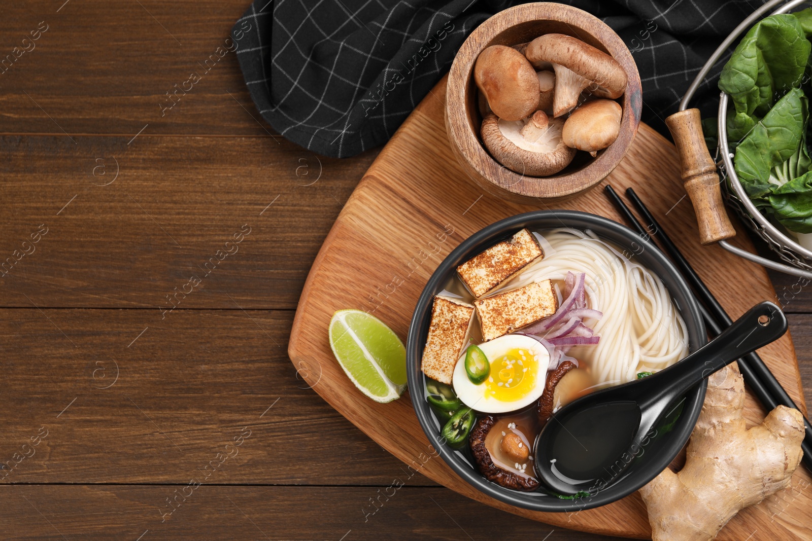 Photo of Delicious vegetarian ramen and products on wooden table, flat lay. Space for text