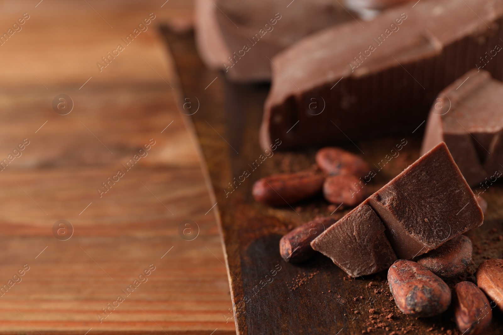 Photo of Pieces of tasty milk chocolate, powder and cocoa beans on wooden table, closeup. Space for text