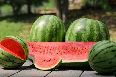 Photo of Different ripe whole and cut watermelons on wooden table outdoors