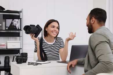Photo of Young professional photographer holding camera while talking with man in modern photo studio