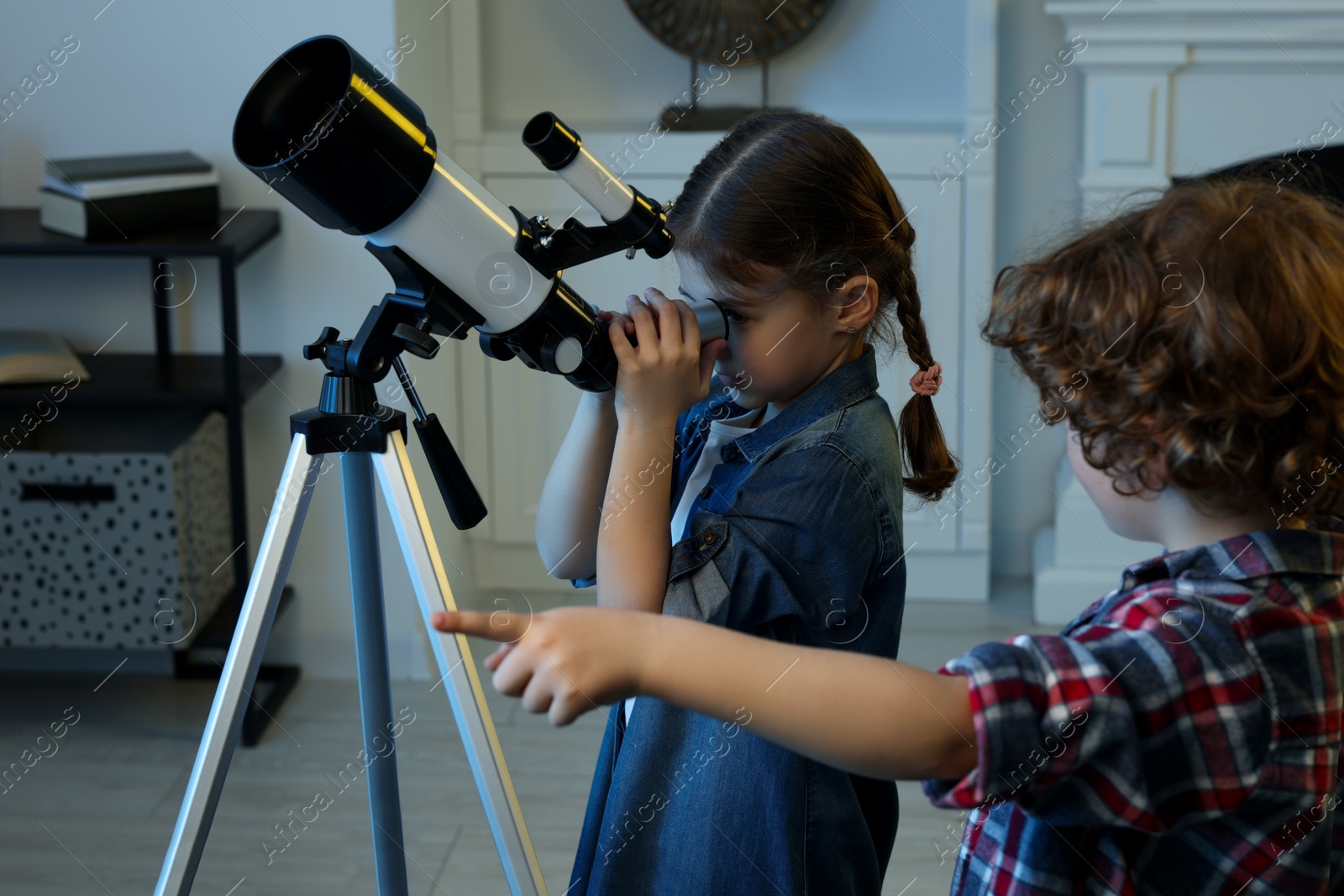 Photo of Cute little children using telescope to look at stars in room