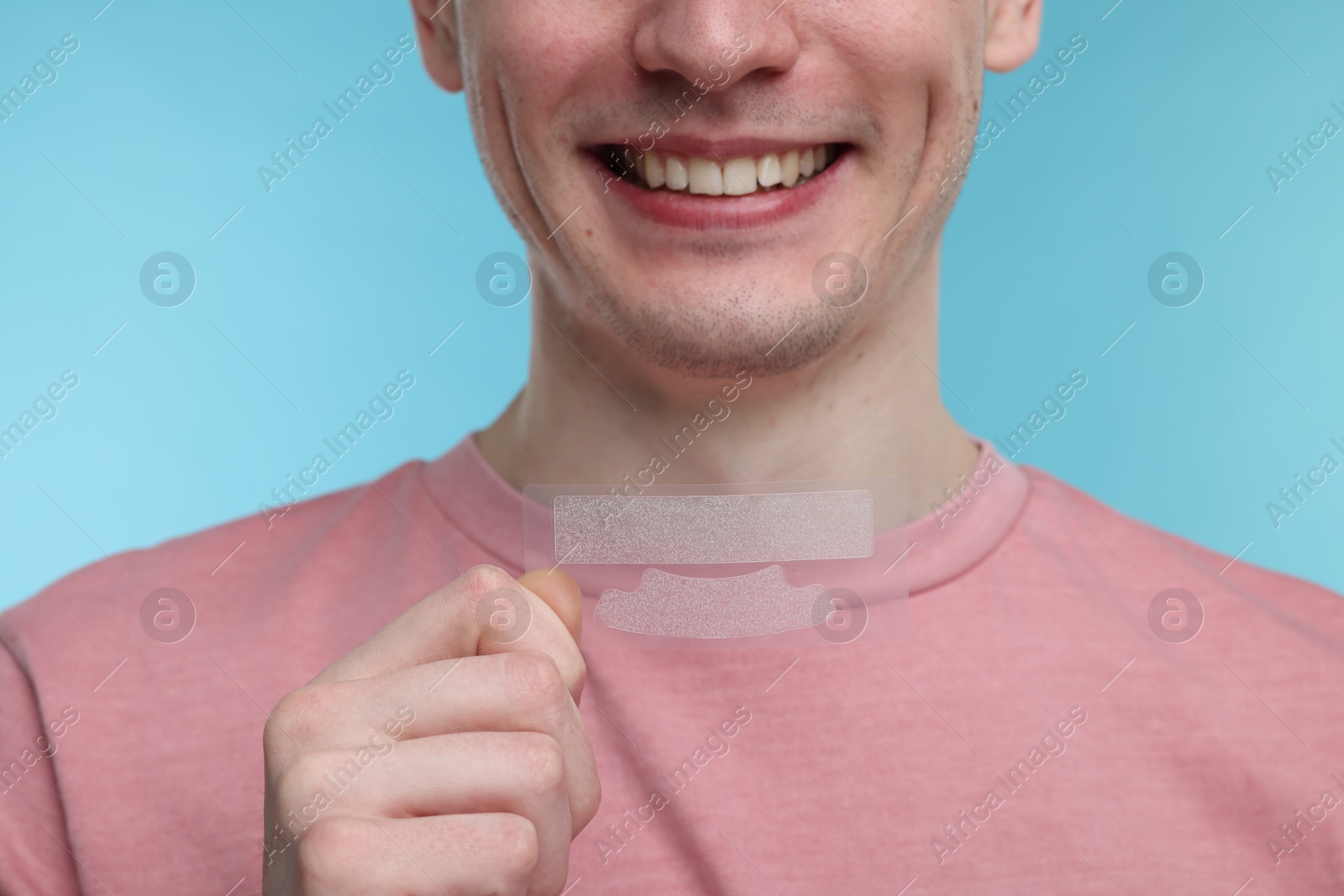 Photo of Young man with whitening strips on light blue background, closeup