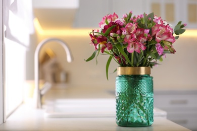 Vase with beautiful alstroemeria on countertop in kitchen, space for text. Interior design