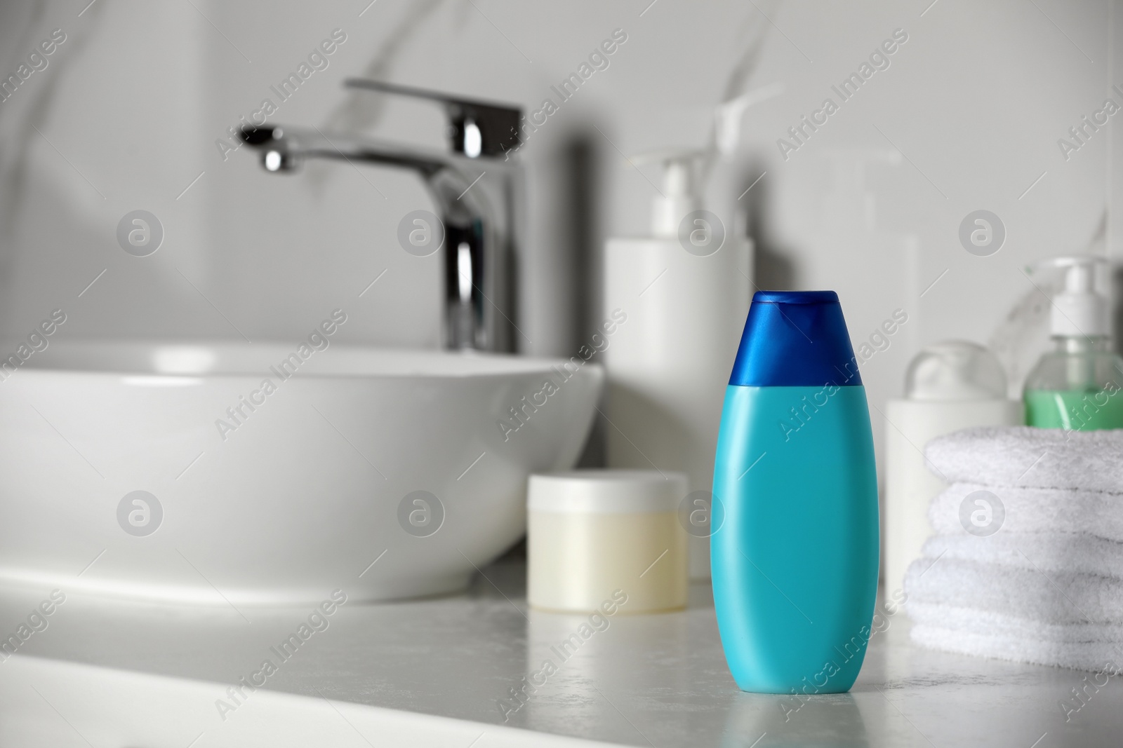 Photo of Bottle of shampoo and stacked towels near sink on bathroom counter, space for text
