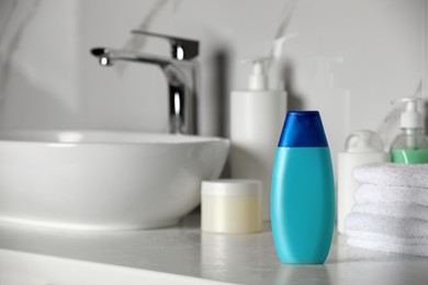 Bottle of shampoo and stacked towels near sink on bathroom counter, space for text