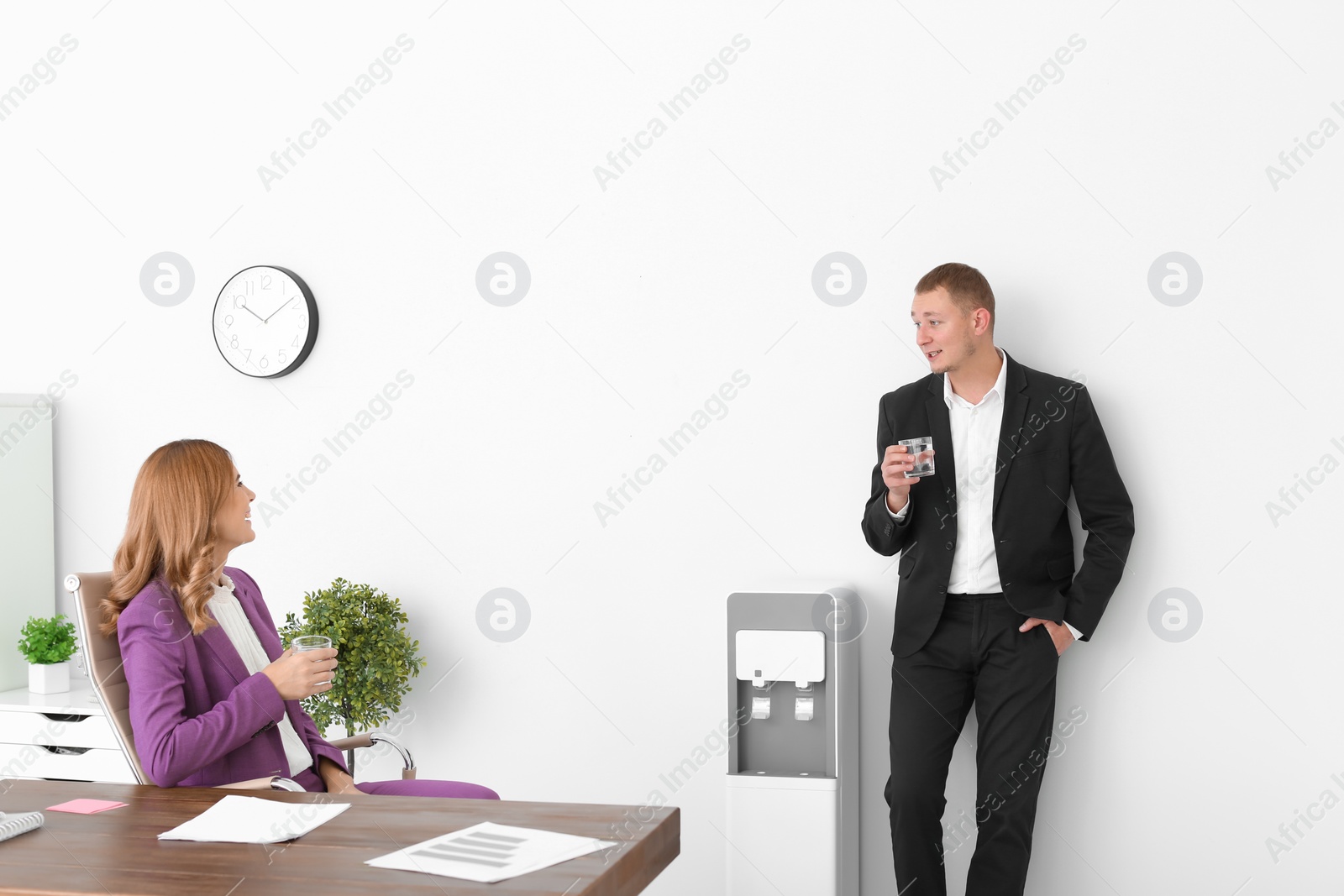 Photo of Co-workers having break near water cooler at workplace. Space for text