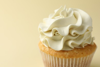 Tasty vanilla cupcake with cream on pale yellow background, closeup. Space for text