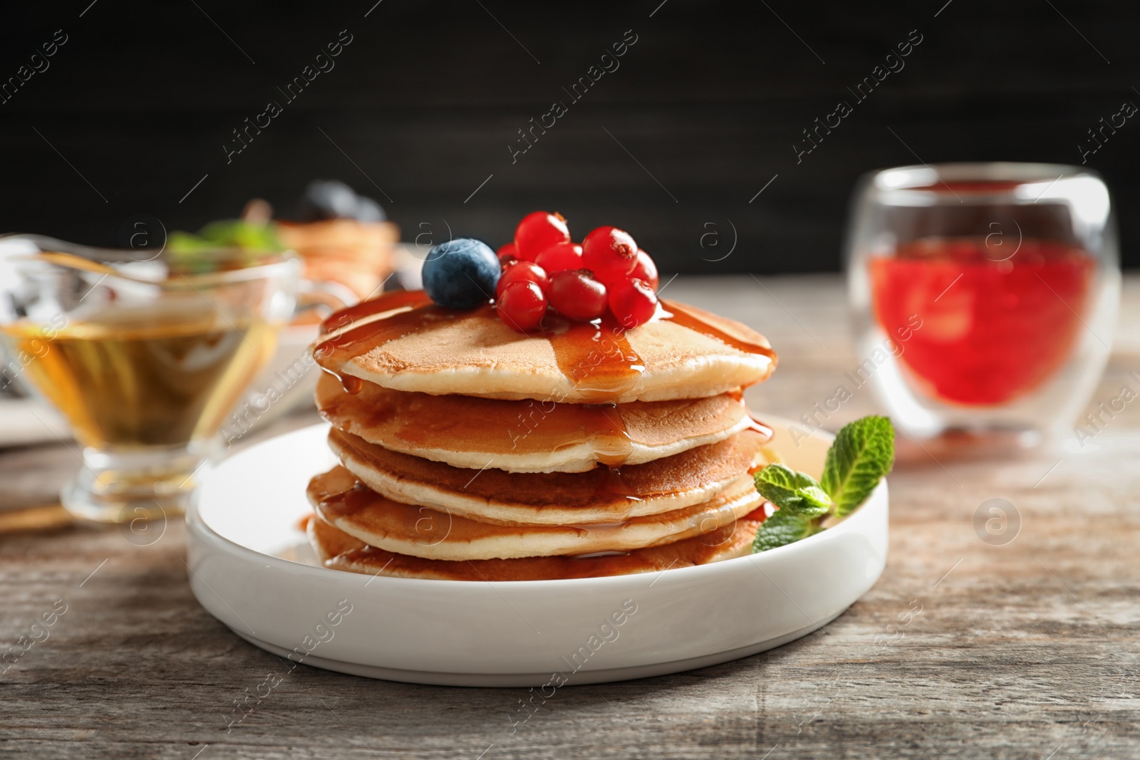 Photo of Stack of tasty pancakes with berries and syrup on table