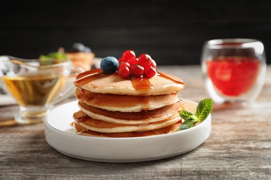 Stack of tasty pancakes with berries and syrup on table