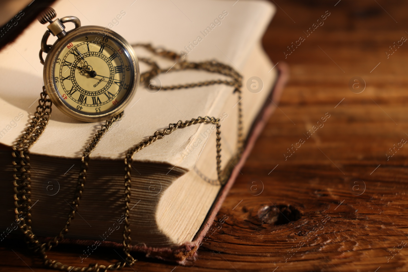 Photo of Pocket clock with chain and book on wooden table, closeup. Space for text