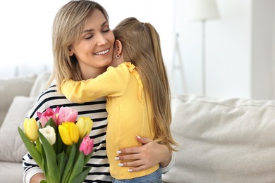 Photo of Little daughter congratulating her mom with Mother`s Day at home, space for text. Woman holding bouquet of beautiful tulips