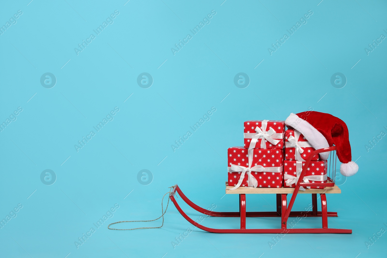 Photo of Stylish sleigh with Christmas gifts and Santa hat on light blue background, space for text